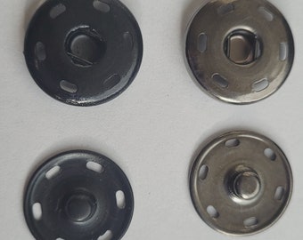 Puede incluir: Cuatro botones a presión de metal, dos negros y dos plateados, con un diseño circular y múltiples agujeros alrededor del borde.