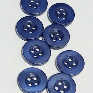 May include: Eight navy blue buttons are displayed. Each button is circular with four holes in the centre for stitching. The buttons have a slightly raised edge and a smooth, matte finish. Suitable for various sewing projects.