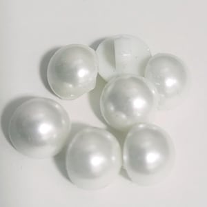 May include: A collection of white, pearlescent beads of varying sizes. The beads have a smooth, reflective surface, and are arranged on a white background. One bead is a white button with a shank.