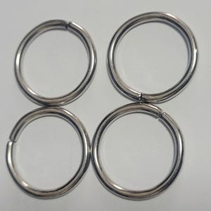 Pu&ograve; includere: Quattro anelli metallici argentati, ciascuno dei quali forma un cerchio completo con una piccola apertura. Gli anelli sono disposti a quadrato, due in alto e due in basso. Gli anelli sono in metallo lucido.