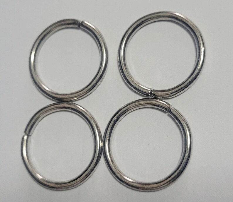 Pu&ograve; includere: Quattro anelli metallici argentati, ciascuno dei quali forma un cerchio completo con una piccola apertura. Gli anelli sono disposti a quadrato, due in alto e due in basso. Gli anelli sono in metallo lucido.