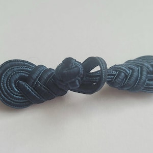 K&ouml;nnte beinhalten: Ein dunkelblauer Stoffknoten, auch bekannt als chinesischer Knoten, ist ein dekoratives Element, das f&uuml;r Kleidung oder Wohnaccessoires verwendet wird.