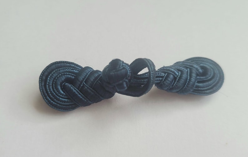 K&ouml;nnte beinhalten: Ein dunkelblauer Stoffknoten, auch bekannt als chinesischer Knoten, ist ein dekoratives Element, das f&uuml;r Kleidung oder Wohnaccessoires verwendet wird.