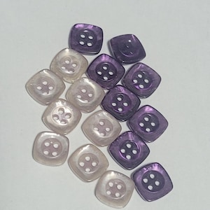 May include: A collection of square-shaped buttons in two colors: iridescent pearl and deep purple. Each button has four holes for sewing. The buttons are arranged on a white surface, suitable for sewing projects.