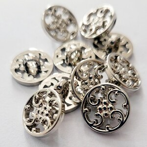 May include: A collection of round, silver-toned metal buttons featuring an intricate, openwork filigree design. Each button has a raised, polished surface with a central cluster of small dots surrounded by swirling, curved cut-out patterns.