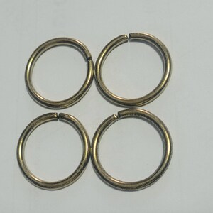 Pu&ograve; includere: Quattro anelli divisi color oro, ciascuno con un piccolo spazio per attaccare oggetti. Gli anelli sono circolari e hanno una superficie leggermente strutturata. Sono disposti a quadrato su uno sfondo semplice.