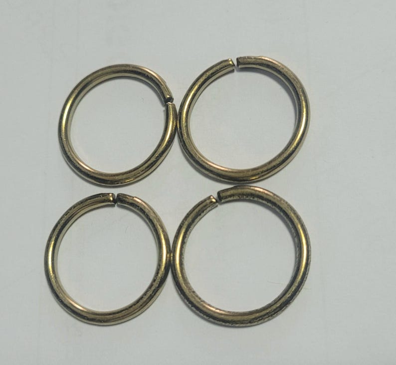 Pu&ograve; includere: Quattro anelli divisi color oro, ciascuno con un piccolo spazio per attaccare oggetti. Gli anelli sono circolari e hanno una superficie leggermente strutturata. Sono disposti a quadrato su uno sfondo semplice.