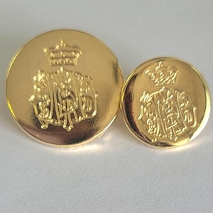May include: Two gold-coloured metal buttons with a raised design. The larger button features a crown and a monogram. The smaller button is a smaller version of the larger button.