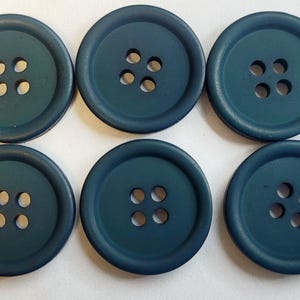 May include: Six teal-colored buttons with four holes each, arranged in two rows of two. The buttons are round with a slightly raised edge and a matte finish. The buttons are on a white surface.