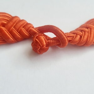K&ouml;nnte beinhalten: Ein Paar orangefarbene Stoffkn&ouml;pfe oder -verschl&uuml;sse, die oft f&uuml;r Kleidung oder Bastelarbeiten verwendet werden.