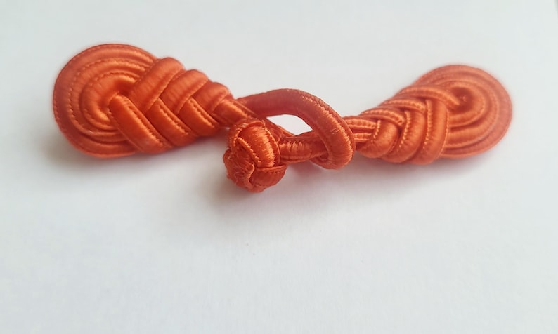 K&ouml;nnte beinhalten: Ein Paar orangefarbene Stoffkn&ouml;pfe oder -verschl&uuml;sse, die oft f&uuml;r Kleidung oder Bastelarbeiten verwendet werden.