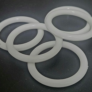 May include: Four white, circular rubber O-rings are arranged on a dark surface. The rings are smooth and have a consistent thickness. The O-rings are likely used for sealing or as components in machinery or equipment.