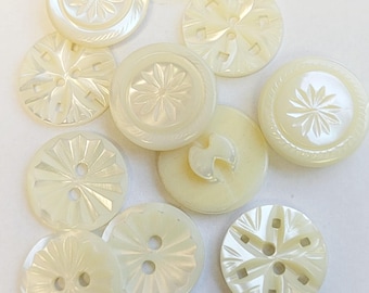 May include: A collection of 10 white mother of pearl buttons with various carved designs. The buttons are round and have two holes.