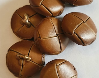 May include: A collection of brown, round buttons with a woven leather-like design. Each button has a metal loop on the back for sewing. The buttons are arranged on a white surface.
