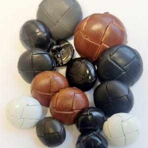 Peut inclure: Un assortiment de boutons ronds de différentes tailles et couleurs, dont noir, marron, gris et blanc. Chaque bouton présente un motif segmenté cousu. Les boutons sont disposés sur un fond blanc.