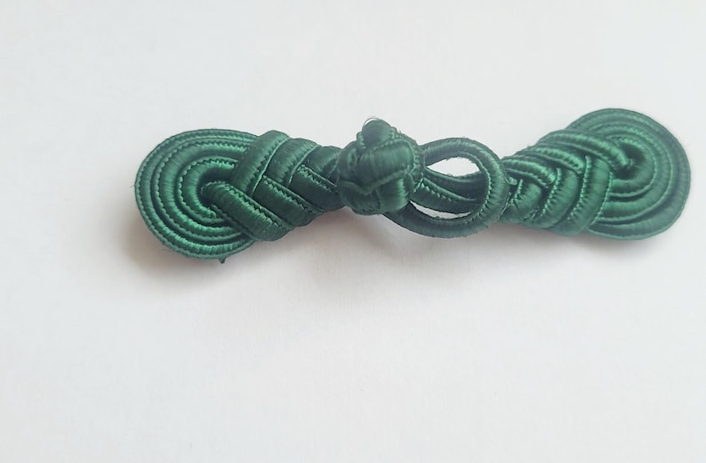 K&ouml;nnte beinhalten: Ein dunkelgr&uuml;ner Stoffknoten, auch bekannt als chinesischer Knoten, ist ein dekoratives Element f&uuml;r Kleidung oder Kunsthandwerk.