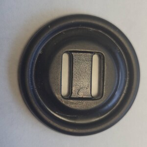 May include: A black plastic button with a double slot opening. The button has a raised outer edge.