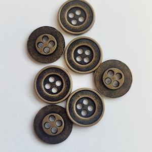 May include: Seven antique gold-toned buttons, each with four holes. The buttons are round and have a raised edge.