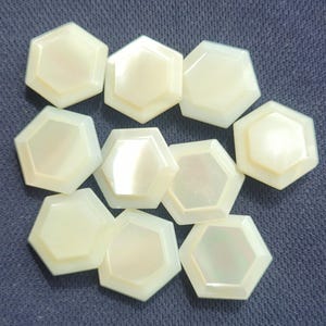 May include: Nine white iridescent hexagonal buttons with a slightly raised edge.