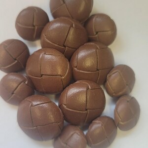 Peut inclure: Un groupe de boutons en cuir marron avec un motif tissé. Les boutons sont disposés en pile, certains se chevauchant.