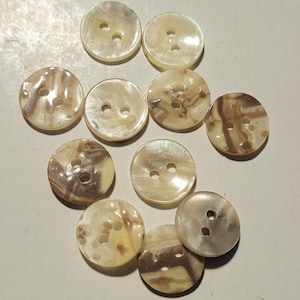 May include: A collection of round, iridescent buttons with two holes each. The buttons have a creamy white base color with brown and tan marbling. These decorative buttons are suitable for sewing and craft projects.