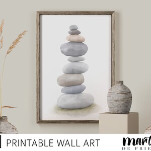 May include: A printable wall art print featuring a stack of grey and beige stones in a minimalist style. The stones are stacked in a zen-like formation, creating a calming and serene atmosphere.