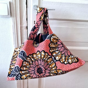 Peut inclure: Un sac fourre-tout corail avec un motif floral marron, noir et blanc. Le sac présente un motif répété de grandes fleurs et de feuilles. Le sac est suspendu à une poignée de porte argentée.