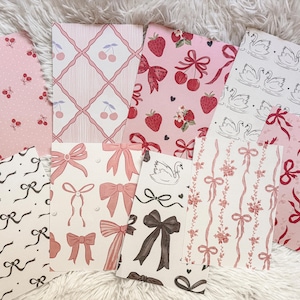 Könnte beinhalten: Eine Sammlung von Papieren mit verschiedenen Mustern. Die Muster umfassen Kirschen, Erdbeeren, Schleifen und Schwäne in Rosa, Rot und Schwarz. Einige Papiere haben Punkte oder Gittermuster.
