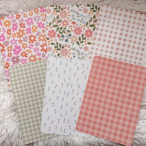 Könnte beinhalten: Eine Sammlung von Papieren mit Mustern. Die Blätter zeigen Blumen- und Vichy-Designs in Pink, Orange, Grün und Weiß. Die Blumenmuster umfassen verschiedene Blumenarten, während die Vichy-Muster ein klassisches Karomuster aufweisen.