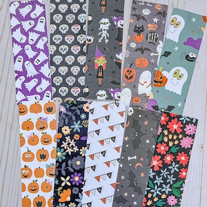 May include: A collection of colorful Halloween and floral-themed bookmarks. Designs include ghosts, skulls, pumpkins, bats, and flowers. The bookmarks are rectangular with rounded corners and various patterns and colors.