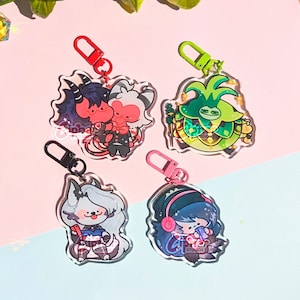 May include: Four colorful character keychains with clear acrylic backgrounds. The characters are a green plant monster, a red and black demon, a white wolf, and a blue-haired girl with headphones.