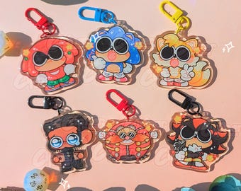 Könnte beinhalten: Eine Sammlung von sechs Schlüsselanhängern aus Acryl mit Cartoon-Charakteren mit großen Augen. Die Schlüsselanhänger haben verschiedene Farben und Designs, mit roten, blauen, gelben und schwarzen Akzenten. Jeder Schlüsselanhänger hat einen Metallverschluss.