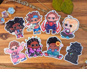 May include: Eight colorful cartoon character stickers featuring different expressions and poses. The stickers are on a wooden surface with lavender and leaves.