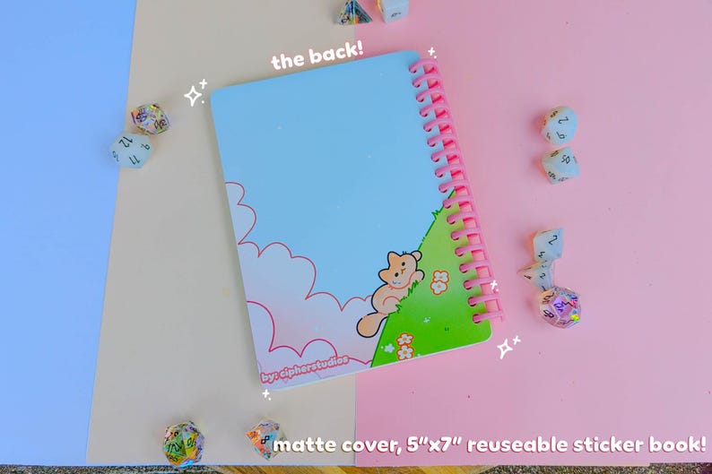 May include: A matte cover, 12.7cm x 17.8cm reusable sticker book with a light blue sky design and a pink spiral binding. The cover features a cartoon cat on a green hill. The text "the back!" is visible.