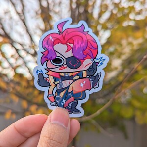 May include: A sticker featuring a cartoon character with pink and purple hair, wearing a yellow and black outfit with a red eyepatch. The character is holding a glowing blue object in their right hand and has a surprised expression on their face.