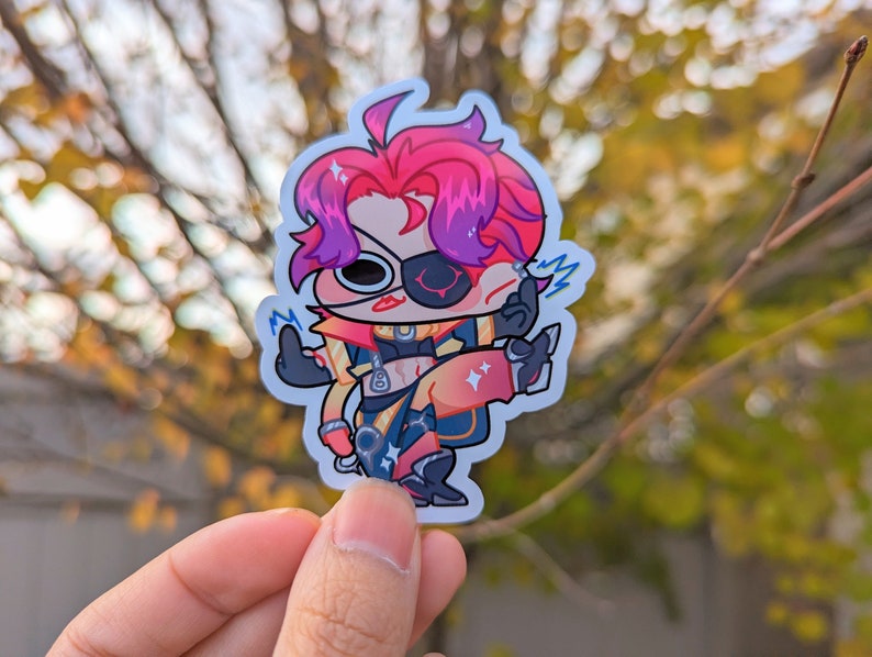 May include: A sticker featuring a cartoon character with pink and purple hair, wearing a yellow and black outfit with a red eyepatch. The character is holding a glowing blue object in their right hand and has a surprised expression on their face.