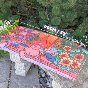 May include: A rectangular desk mat with a colorful illustration of a cat in a hat, sunflowers, and a window scene. The mat measures 35 inches long and 15 inches wide. The design features shades of pink, orange, and green.
