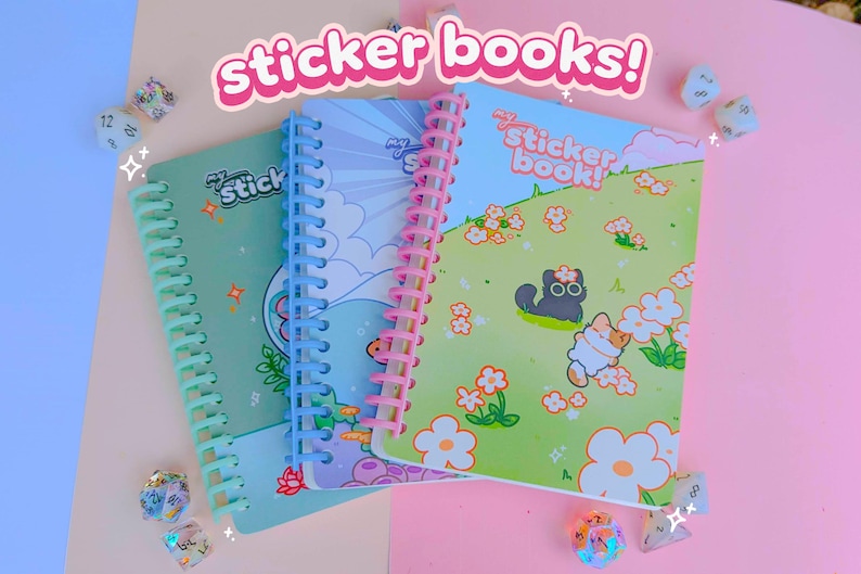 May include: Three spiral-bound sticker books with colourful covers. The covers feature illustrations of a cat, flowers, and other cute designs. The text "sticker books!" is displayed above the books. Dice are scattered around the books.