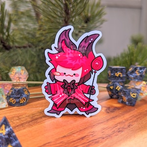May include: A red and white cartoon character sticker with a lollipop. The character has horns, a bow tie, and a red suit. The sticker is on a wooden surface with dice.