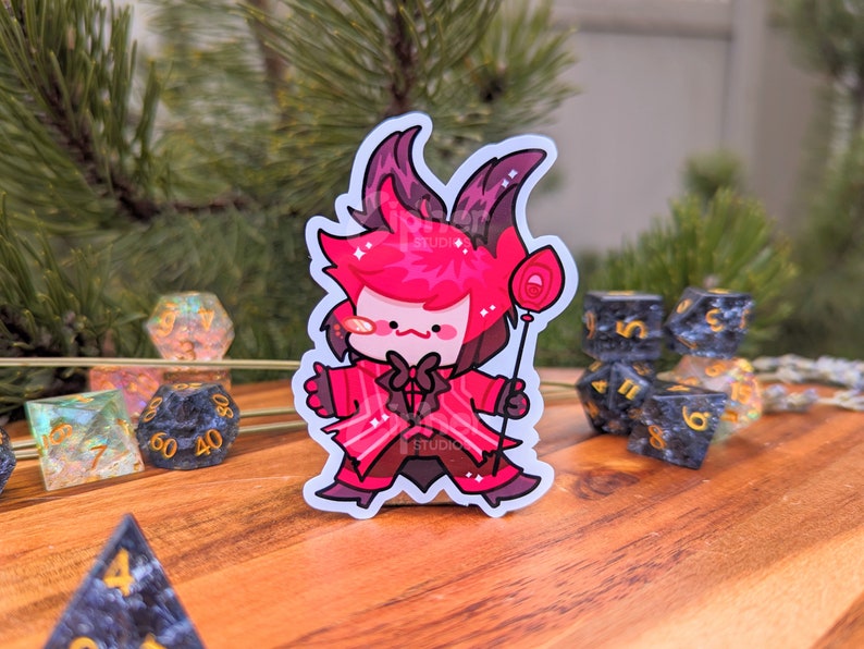 May include: A red and white cartoon character sticker with a lollipop. The character has horns, a bow tie, and a red suit. The sticker is on a wooden surface with dice.