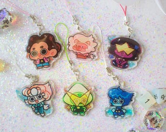 May include: Six acrylic charms featuring cartoon characters with large eyes, including a boy with brown hair, a pink lion, a dark-skinned character with a yellow visor, a character with peach hair, a green character with a yellow visor, and a blue character.
