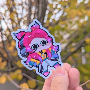 May include: A sticker featuring a cartoon character with pink hair, wearing headphones and a yellow jacket. The character has large eyes and a surprised expression.