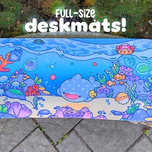 May include: Full-size deskmat with an underwater scene. The design features a blue whale, coral, fish, and other sea creatures. The background is a gradient of blue, and the text "FULL-SIZE deskmats!" is at the top.