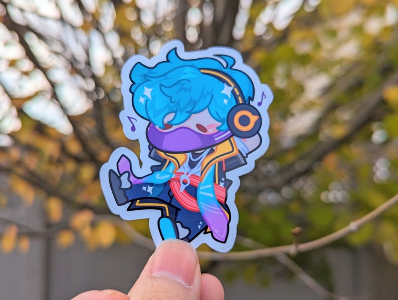 May include: A blue and purple cartoon character sticker with a yellow headband and headphones. The character is wearing a purple mask and has blue hair. The sticker is on a white background.