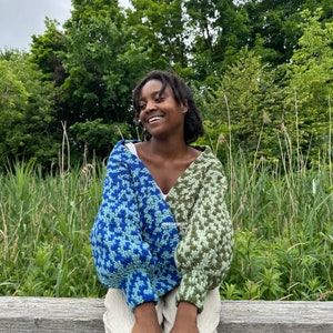 Op de afbeelding: Een persoon draagt ​​een blauw en groen gebreide trui met een witte achtergrond. De trui heeft een uniek ontwerp met een mix van kleuren en texturen.