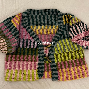May include: A crocheted cardigan with a patchwork design in shades of pink, green, and yellow. The cardigan has a button closure and a cropped length.