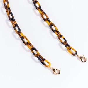 May include: A tortoiseshell chain with gold clasps. The chain is made of plastic and has a linked design.