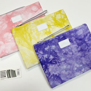 May include: Three tie-dye pattern zipper pouches in pink, yellow, and purple. Each pouch has a white leather label and a matching wrist strap. The pouches are rectangular and have a zipper closure.