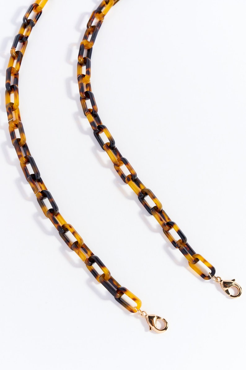 May include: A tortoiseshell chain with gold clasps. The chain is made of plastic and has a linked design.