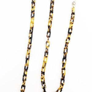 May include: A long, brown and yellow chain with a tortoiseshell pattern. The chain has two gold clasps at the ends.